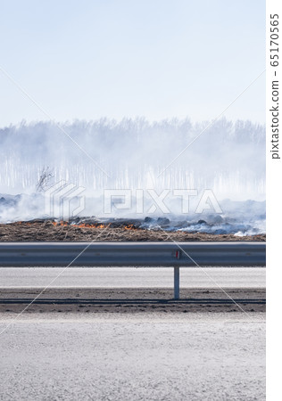 a strong fire, flame and a lot of smoke near the paved highway route, burning dry grass 65170565