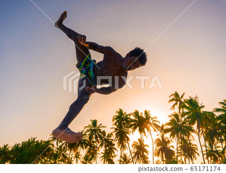 Young Attractive Muscular and Strong Athletic Black African Man at the White Sand Beach Training Acrobatics and Jumping Gymnastics Beach Performance at sunset time Young Attractive Muscular and Strong Athletic Black African Man at the White Sand Beach Training Acrobatics and Jumping Gymnastics Beach Performance at sunset time 65171174