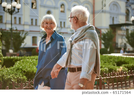 I love my husband. Happy and beautiful elderly couple holding hands and looking at each other while walking outdoors I love my husband. Happy and beautiful elderly couple holding hands and looking at each other while walking outdoors 65171564