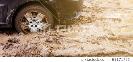 The car got stuck on a dirt road in the mud. Wheel of a car stuck in the mud on the road. Car on a 65171795