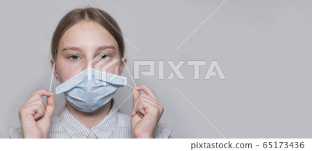 teenager girl 12-15 years old, removes medical mask, end of virus, disease gone, recovery and freedom, child recovered, free space for copy text. Flu infection disease and pandemic. Gray background. 65173436
