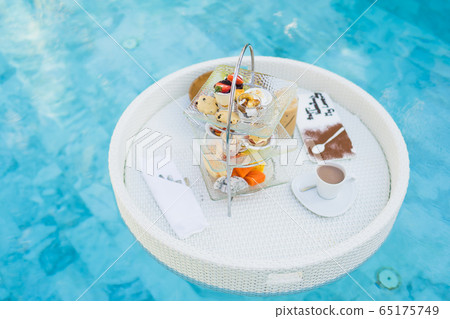 Breakfast and afternoon tea set floating around swimming pool Breakfast and afternoon tea set floating around swimming pool 65175749