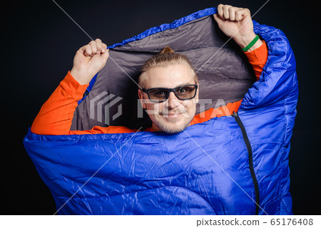 A young guy in sunglasses posing in a sleeping bag A young guy in sunglasses posing in a sleeping bag 65176408