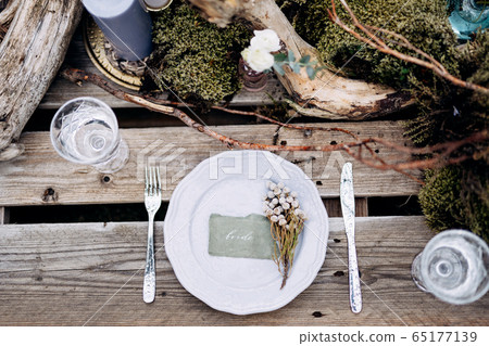 Wedding dinner table reception. An impromptu table for two of the construction pallet on grey grass in Iceland. Light purple plate, snags, moss, purple candles, lavender, bouquet of flowers. Top view Wedding dinner table reception. An impromptu table for two of the construction pallet on grey grass in Iceland. Light purple plate, snags, moss, purple candles, lavender, bouquet of flowers. Top view 65177139