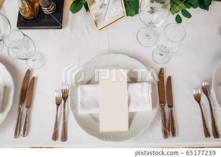 Wedding dinner table reception. The cream sheet of the menu is in a plate with a cloth napkin. Cutlery laid out according to the rules of etiquette. Top View  65177239
