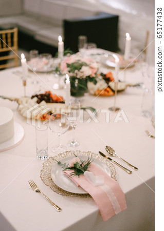 Wedding dinner table reception. Gold plate under white, pink fabric towel, pink flower with silk ribbon on top. Cutlery next to the plate. Top view 65177438