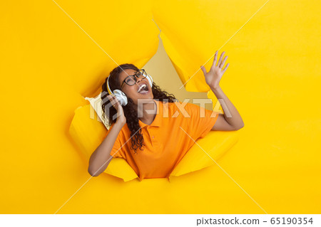 Cheerful young woman poses in torn yellow paper hole background, emotional and expressive 65190354