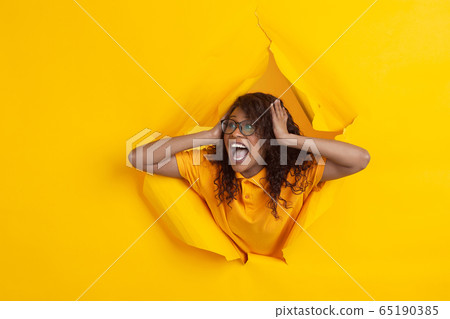 Cheerful young woman poses in torn yellow paper hole background, emotional and expressive 65190385