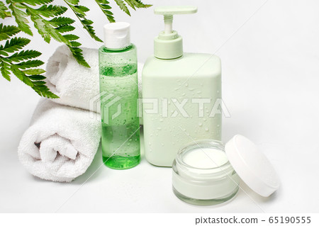 Cosmetic containers with green herbal leaves, blank label package for branding mock-up. Moisturizing cream, liquid soap or shampoo, tonic, face and body skin care. Natural organic beauty product. 65190555