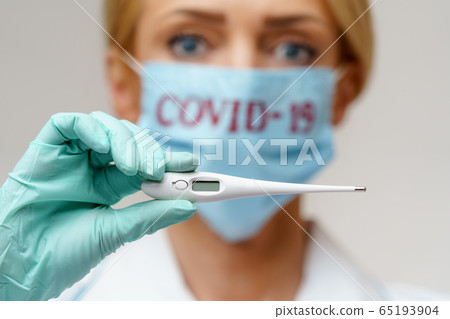 medical doctor nurse woman wearing protective mask and rubber or latex gloves - holding thermometer medical doctor nurse woman wearing protective mask and rubber or latex gloves - holding thermometer 65193904