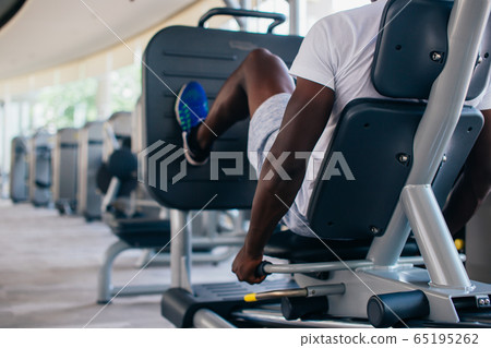 Back view of African American man doing exercise on leg press during fitness training in modern gym 65195262