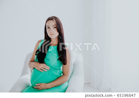 a pregnant woman before childbirth sits in white couch 65196847