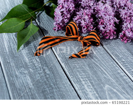 St. George's ribbon on a natural wooden background next to a branch of lilac, a symbol of Victory Day on may 9. 65198221