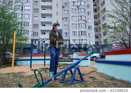 teen boy stands by seesaw on playground near teen boy stands by seesaw on playground near 65198630