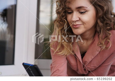 Cheerful gorgeous young woman with curly hair with smartphone 65199202