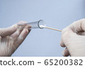 Glass test tube and cotton swab in the hands of a scientist. A virologist in rubber disposable gloves holds a laboratory flask and for analysis. He took a smear sample for a coronavirus test 65200382