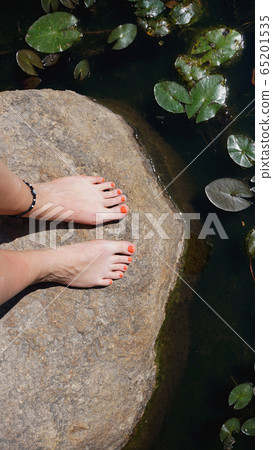 Woman feet on stone near pond - Summer vacation concept Woman feet on stone near pond - Summer vacation concept 65201535