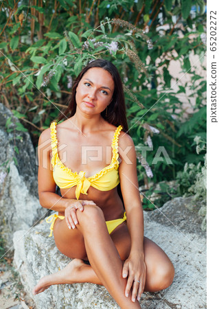 Beautiful woman with long hair in yellow swimsuit sunbathes on the beach by the sea Beautiful woman with long hair in yellow swimsuit sunbathes on the beach by the sea 65202272