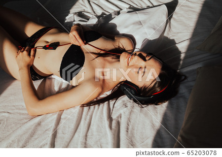 woman brunette listens to music with headphones lying on the bed woman brunette listens to music with headphones lying on the bed 65203078