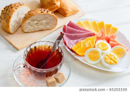 Fresh delicious breakfast with soft boiled egg, cheese, ham fresh bread and cup coffee or tea on light wooden background. 65203339