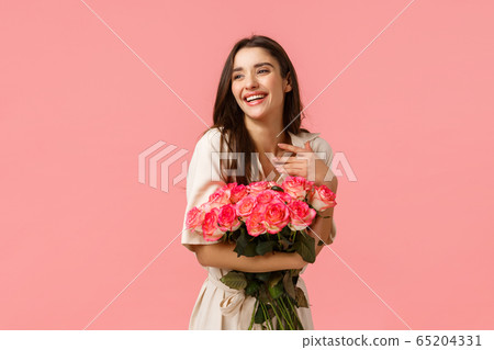 Happiness, romance and beauty concept. Cheerful gorgeous brunette girl in dress, holding roses and smiling flattered, touch chest laughing look away blushing, standing pink background enthusiastic Happiness, romance and beauty concept. Cheerful gorgeous brunette girl in dress, holding roses and smiling flattered, touch chest laughing look away blushing, standing pink background enthusiastic 65204331