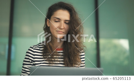 Attractive young woman with long curly hair wearing striped shirt is sitting on stairs of building Attractive young woman with long curly hair wearing striped shirt is sitting on stairs of building 65205113