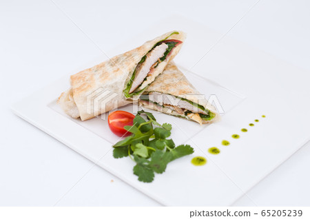 Shawarma chicken roll in a pita with fresh vegetables and cream sauce on white background. Selective focus Shawarma chicken roll in a pita with fresh vegetables and cream sauce on white background. Selective focus 65205239