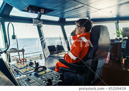 Filipino deck Officer on bridge of vessel or ship. He is speaking on GMDSS VHF radio 65209439