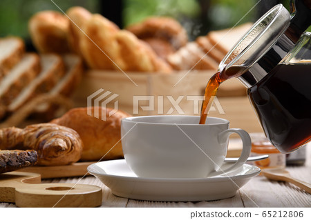 Pouring coffee with smoke on a cup with breads or bun, croissant and bakery on white wooden table 65212806
