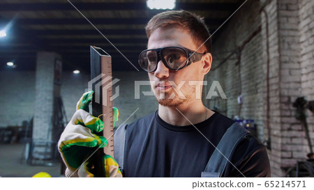Young handsome man in protective glasses looking at the metal detail he made 65214571