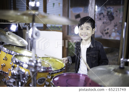 A cute Asian kindergarten boy is enjoying learning to play the drums in a music practice room. 65215749