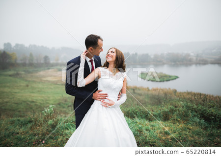 Romantic, fairytale, happy newlywed couple hugging and kissing in a park, trees in background 65220814