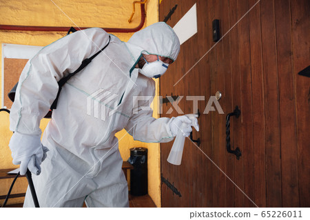Coronavirus Pandemic. A disinfector in a protective suit and mask sprays disinfectants in the house or office Coronavirus Pandemic. A disinfector in a protective suit and mask sprays disinfectants in the house or office 65226011