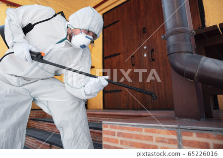 Coronavirus Pandemic. A disinfector in a protective suit and mask sprays disinfectants in the house or office Coronavirus Pandemic. A disinfector in a protective suit and mask sprays disinfectants in the house or office 65226016