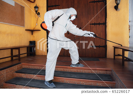 Coronavirus Pandemic. A disinfector in a protective suit and mask sprays disinfectants in the house or office Coronavirus Pandemic. A disinfector in a protective suit and mask sprays disinfectants in the house or office 65226017