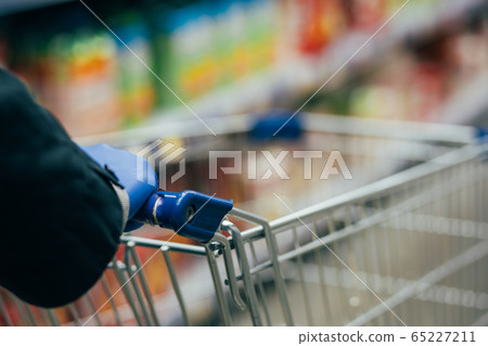 Man in white gloves rolls a cart in the store. epidemic safety. hands in gloves holding basket. 65227211