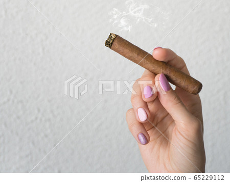 Woman hand holding a burning cigar. Woman hand holding a burning cigar. 65229112