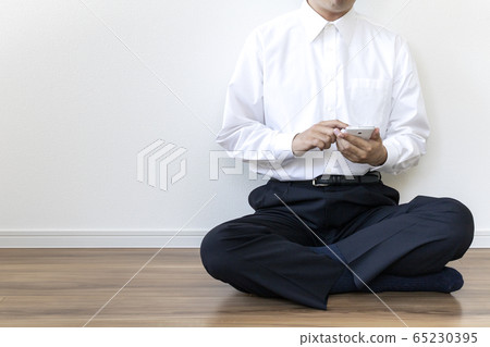 一個穿著襯衫坐在地板上，操作智能手機的人 65230395