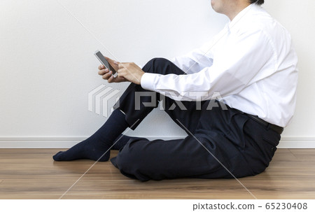 一個穿著襯衫坐在地板上，操作智能手機的人 65230408