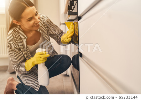 Positive delighted brunette girl cleaning her kitchen 65233144