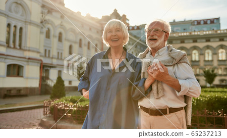 Happy and beautiful senior couple holding hands and smiling while standing outdoors together Happy and beautiful senior couple holding hands and smiling while standing outdoors together 65237213