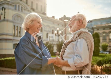 You are my best friend. Happy and beautiful elderly couple holding hands and looking at each other with smile while standing outdoors You are my best friend. Happy and beautiful elderly couple holding hands and looking at each other with smile while standing outdoors 65237214