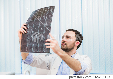 Portrait of a handsome caucasian male radiologist holding x-ray while sitting at his office 65238123
