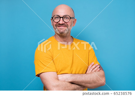 Portrait of smiling man in yellow clothes and glasses. Studio shot on blue wall. 65238576