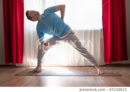 Young caucasian man doing yoga utthita parshvokonasana pose at his living room. 65238615