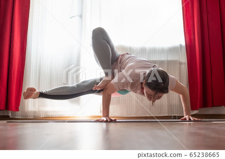 Young woman working out indoors, doing yoga exercise handstand asana 65238665