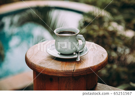 Cup of coffee on wooden table at pool in tropical 65251567
