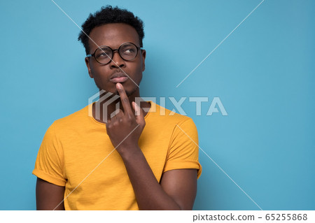 Young african american man, student with finger in mouth in deep thought 65255868