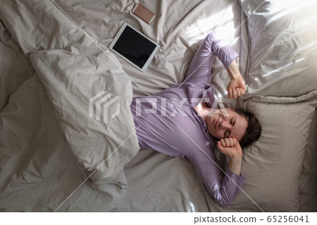 Caucasian young woman waking up and stretching in white bed Caucasian young woman waking up and stretching in white bed 65256041