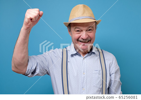 Senior hispanic man in summer hat raising fist up celebrating his success. Senior hispanic man in summer hat raising fist up celebrating his success. 65256081